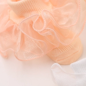 Détail de dentelle superposée et texture en coton côtelé sur des chaussettes bébé pêche