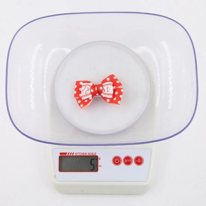 Detail view of 5g red polka dot hair bow with baseball motif on a weighing scale