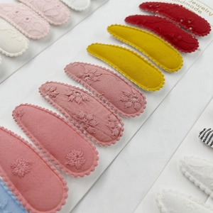 Detail of handmade fabric BB hair clips with delicate floral embroidery and wavy edges