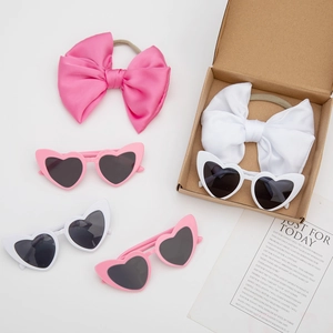 Detailed view of heart sunglasses and satin bow headbands in craft paper gift box packaging