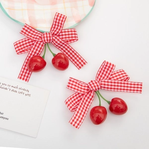 Detail of red gingham cherry hair clips with ribbon bows on a white decorative plate