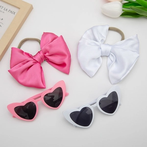 Flat lay of pink and white satin bow headbands with matching heart-shaped sunglasses