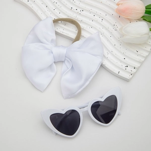 Detail of white satin bow headband and heart-shaped sunglasses for baby girls