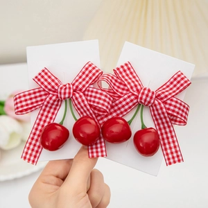 Detailed view of red cherry hair clips with plaid bowknot on white display card