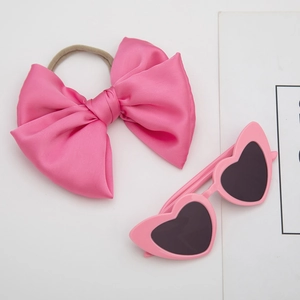 Close-up of pink heart-shaped sunglasses and satin bow headband set for girls