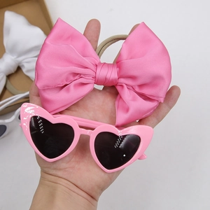 Close-up of pink satin bow headband and heart-shaped sunglasses for baby girls