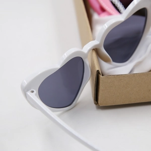 Close-up of white heart-shaped sunglasses with dark lenses and minimalist packaging