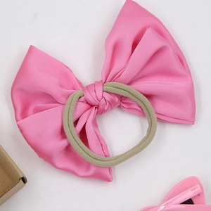 Detailed close-up of a pink satin bow hair tie with high-elasticity band for girls