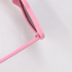 Close-up of metal hinge detail on pink plastic sunglasses for kids with durable screw