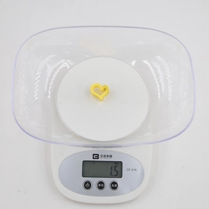 Détail d'une pince à cheveux jaune en forme de cœur pesant 1,5 g sur une balance