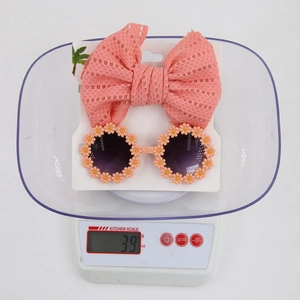 Close-up of children's daisy sunglasses and bow headband set on a digital scale