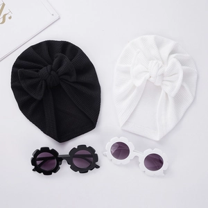 Mise à plat de chapeaux à nœud gaufrés pour bébé et lunettes de soleil fleurs assorties en noir et blanc