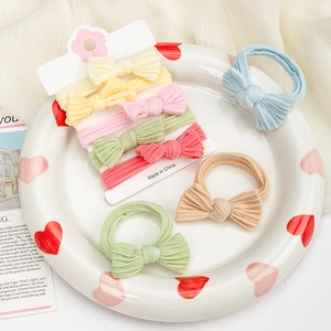 Close-up of five colorful bow hair ties on a ceramic plate showing soft ribbed texture