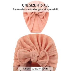 Détail d'un bonnet bébé en maille gaufrée rose pêche montrant sa grande élasticité