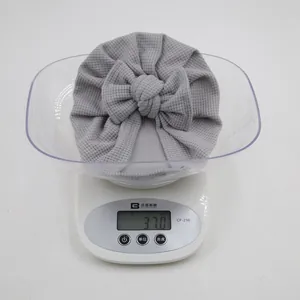 Gros plan d'un bonnet bébé gris à texture gaufre avec gros nœud pesant 37g sur une balance
