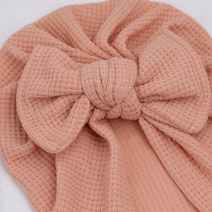 Gros plan du bonnet turban corail pour bébé en maille gaufre avec un grand nœud