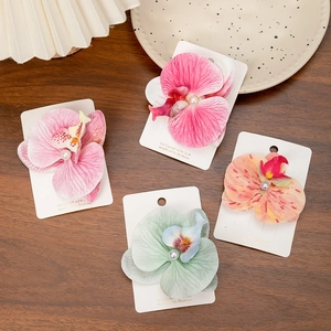 Detail of four colorful silk orchid hair clips with white pearls on a dark wood table