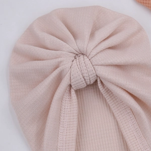 Détail d'un bonnet turban rose pour bébé en tissu gaufré avec un nœud décoratif