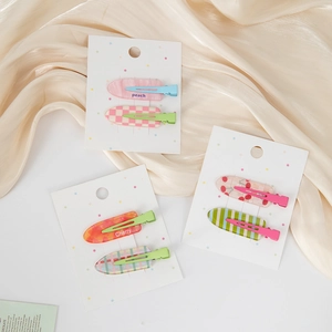 Détail de pinces à cheveux coeur en acétate coloré avec motifs à carreaux et cerises