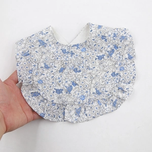 Détail d'un bavoir bébé en coton à fleurs bleues avec bordures en dentelle volantée
