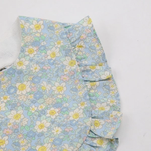 Vue détaillée du bavoir bébé bleu clair avec motif de marguerites jaunes et bord à volants