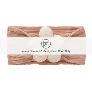 Gros plan d'un bandeau tricoté rose pour bébé avec fleur 3D blanche et maille torsadée