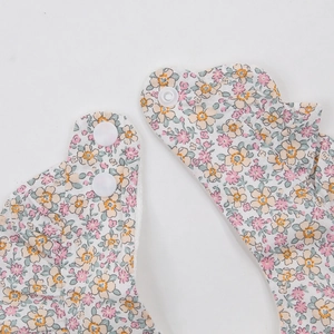 Détail du bavoir fleuri pour bébé avec boutons-pression et bordure à volants élégante