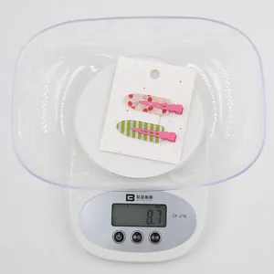 Détail de deux pinces à cheveux coeur colorées sur carte pesant 8,7g sur une balance