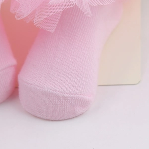 Close-up detail of pink baby socks with delicate chiffon lace trim and soft knit texture