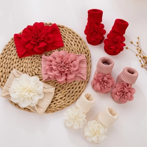 Three-piece baby headband and socks set with large fabric flowers on woven straw mat