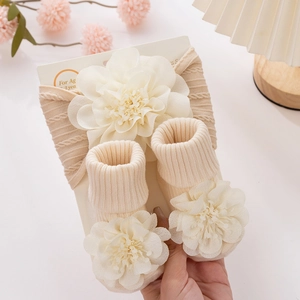 Detailed view of beige knit baby headband and socks set with large white 3D fabric flowers