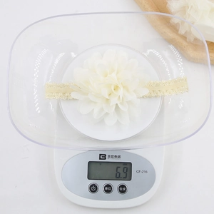 Macro detail of creamy white chiffon flower headband on scale weighing only 6.9 grams