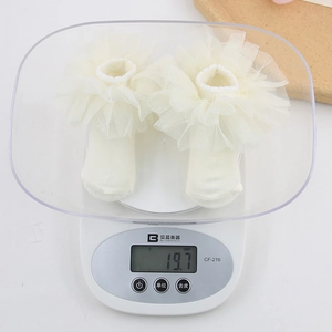 Lightweight cream baby socks with ruffled organza lace showing 19.7g weight on a scale