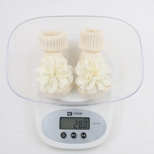 Close-up of beige chiffon flower baby socks on a scale showing lightweight 28g quality
