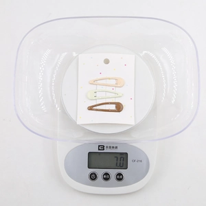 Three colorful teardrop metal hair clips on display card weighing 7.0 grams on a digital scale