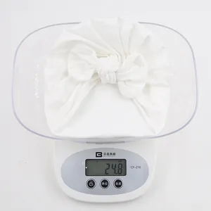 Gros plan détaillé d'un bonnet à nœud blanc pour bébé pesant 24,8 g sur une balance