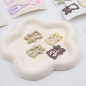 Close-up of matte star hair clips in earthy tones on a white ceramic petal tray