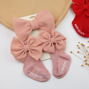 Détail de chaussettes bébé rose et bandeau à nœud assorti sur plateau naturel