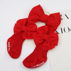 Détail de chaussettes en maille côtelée rouge pour bébé avec grand nœud 3D et texte semelle