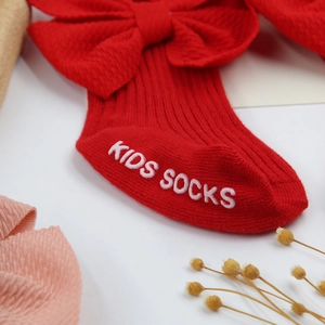Détail de chaussettes bébé rouges à côtes avec gros nœud et semelle antidérapante