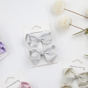 Detail showing two satin bow hair clips in elegant pastel colors on a white card display