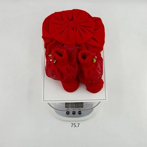 Detailed top view of red newborn cotton hat with bow and lace socks on a scale