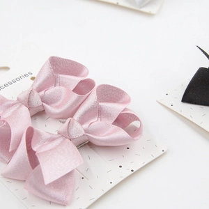 Detail of pink satin bow hair clips on white display card for babies and girls