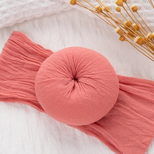 Primer plano de diadema plisada para bebé en rosa coral con nudo de dona en fondo suave