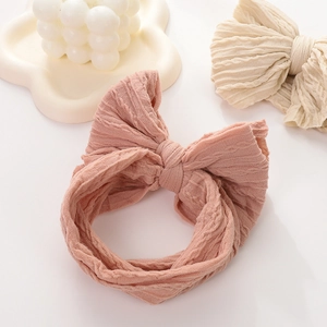 Detail of rose pink baby headband with large bow and ribbed knit texture on cloud tray