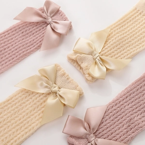 Detail of baby socks with hollow knit texture and decorative satin bows in pink and beige
