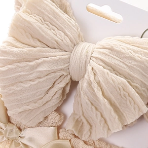 Detailed close-up of beige knitted baby headband with a layered ribbon bow and textures