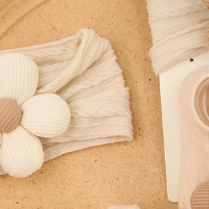 Detail van baby beige gebreide hoofdband met 3D-bloem en bijpassende sokken op kurk oppervlak