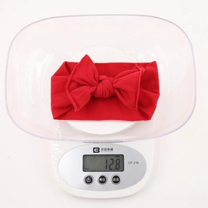 Detailed view of lightweight red bow baby headband on a digital scale weighing 12.8g