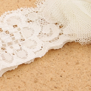 Macro di una fascia per capelli in pizzo bianco con ricami floreali e dettagli in rete
